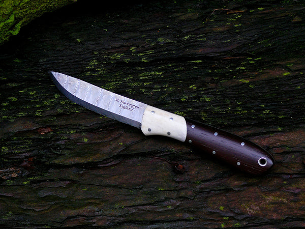Caping Knife.This slim blade is ideal for fine trimming work and fish filleting. The slightly upswept blade itself measures 90mm by 18mm at it's widest point (2.8mm thick) and over all knife length at 195mm. The blade steel is Odins Eye Damasteel with a 27 degree scandi grind.The Sambar Stag bolsters and Rio Rose Wood scales are held on with nickel silver pins and are complemented with a nickel silver thong tube. presented in an oak tanned belt pouch. 